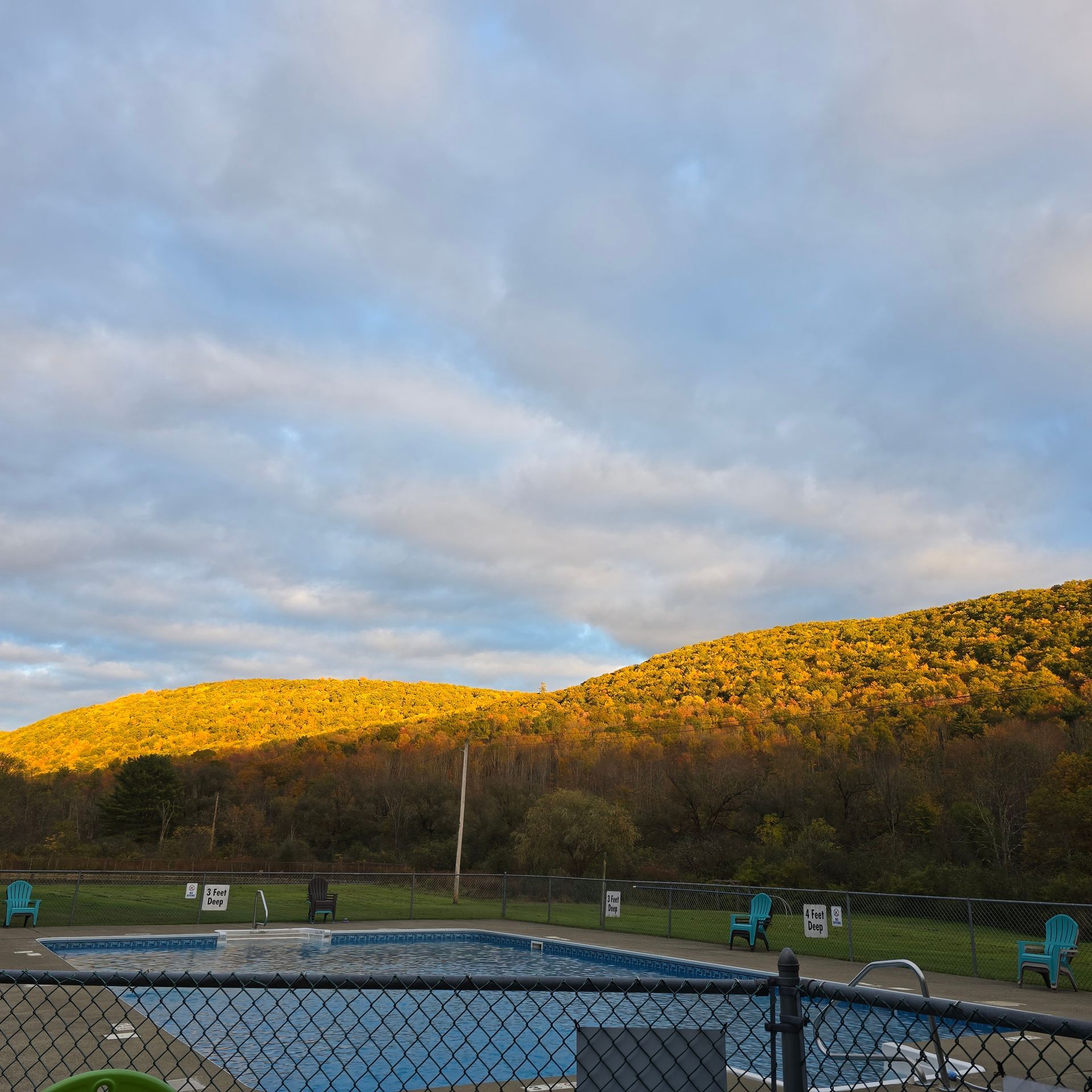 A pool sits in front of golden autumn hills under a partly cloudy sky.