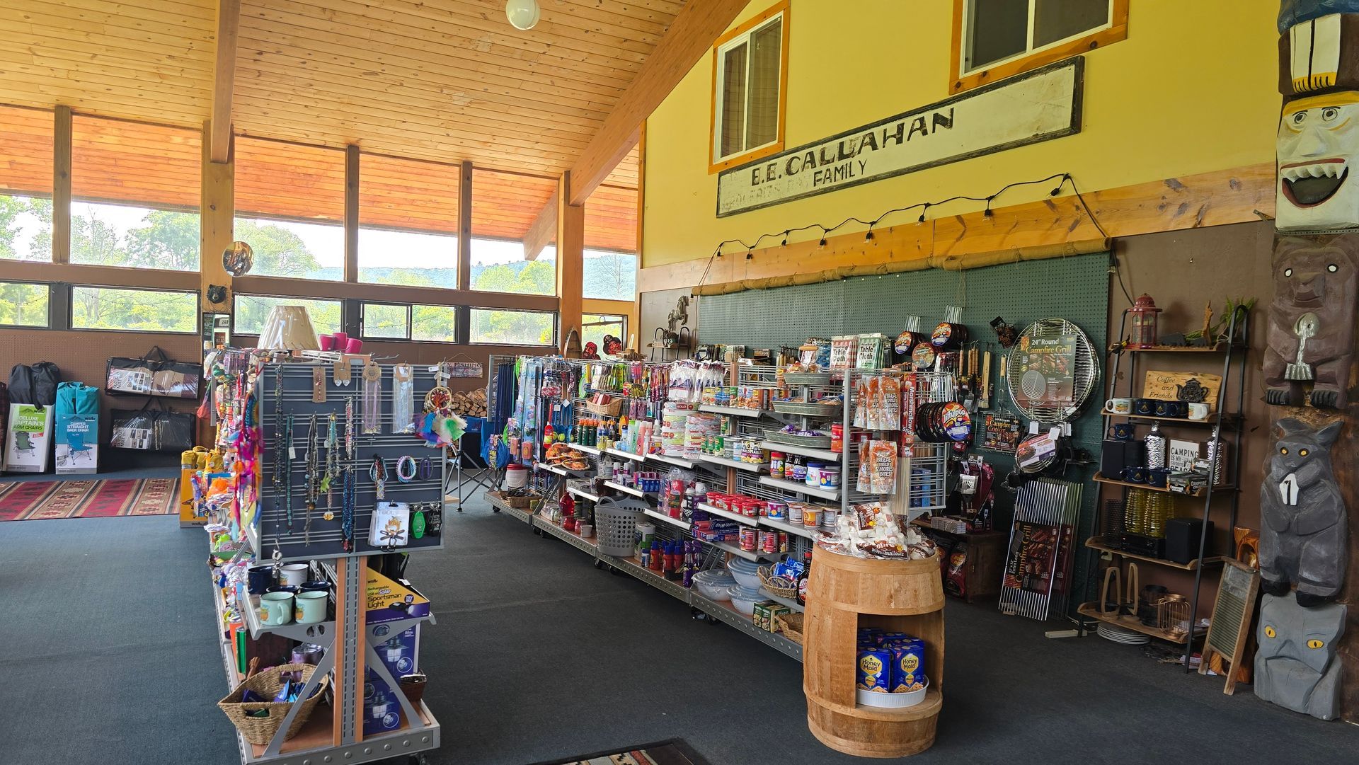 Inside a store: shelves of merchandise, natural wood ceiling, large windows with a view, yellow wall with sign.
