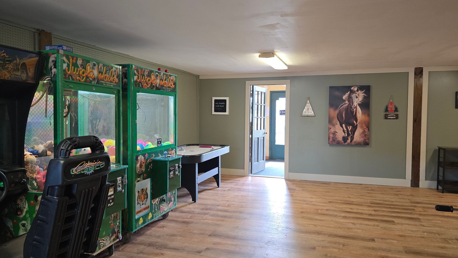 Game room with arcade games, pool table, and open doorway; light green walls and wood floor.
