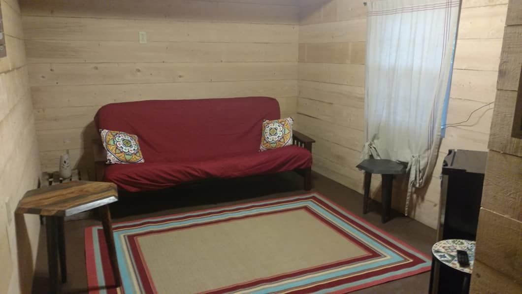 Red futon in a rustic room with wood panel walls, rug, and side tables.