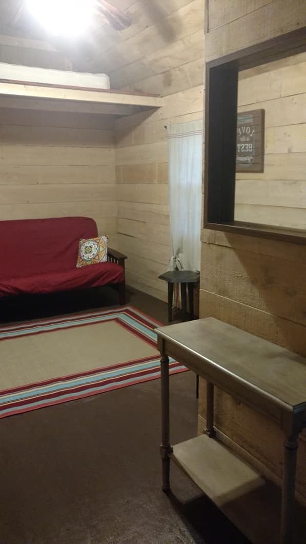 Room with wood-paneled walls, red futon, beige rug, table, and framed art; brown floor.