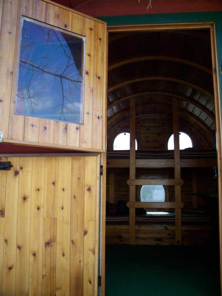 Wooden door open to interior of a wagon with bunks, curved ceiling, and a ladder.