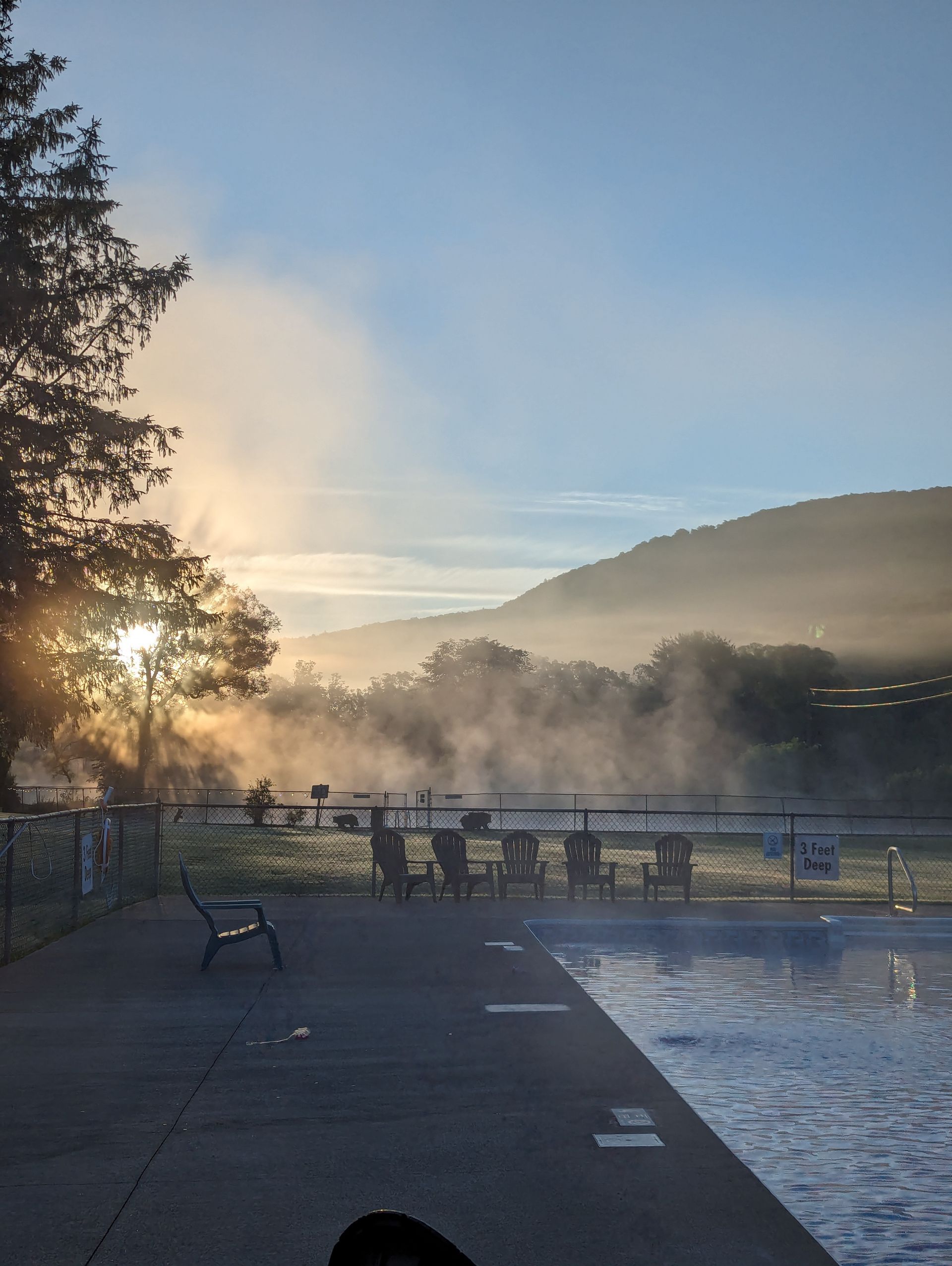 Poolside scene at sunrise with fog over water and mountains in the background.