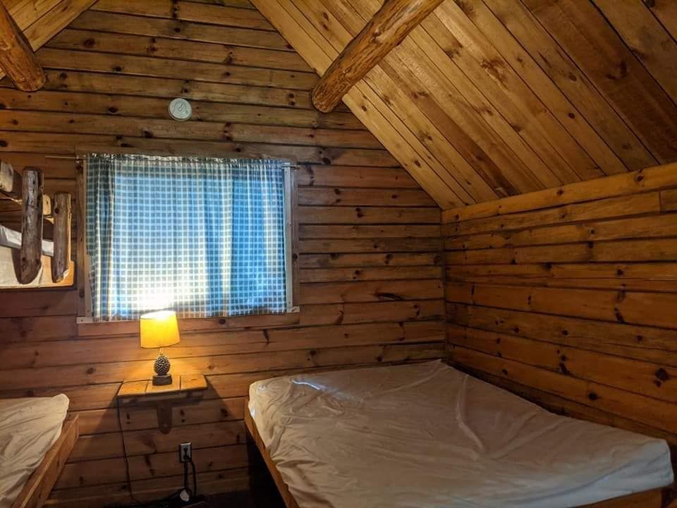 Cozy cabin bedroom with wooden walls, a small window, and two beds with white sheets.