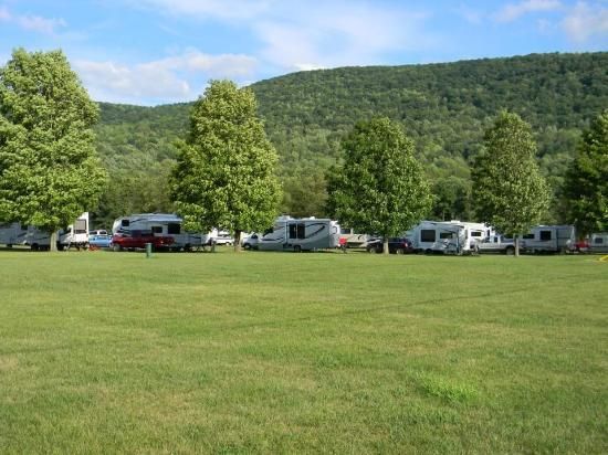 RV campground with campers parked on a grassy field, trees, and a mountain in the background.