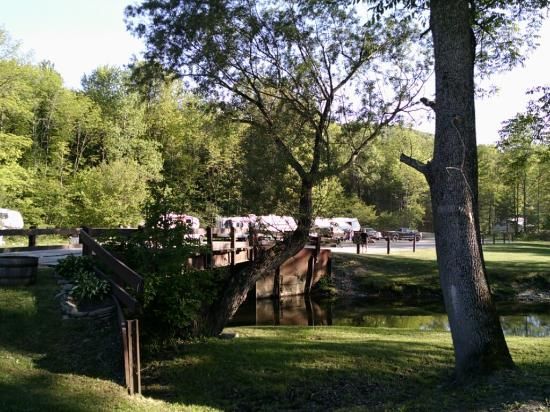 Park scene: A bridge over water, RVs in the background, green trees, and a sunny day.