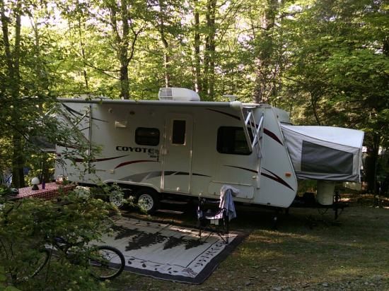 RV with awning extended in a wooded campsite, a rug and bicycle in the foreground.