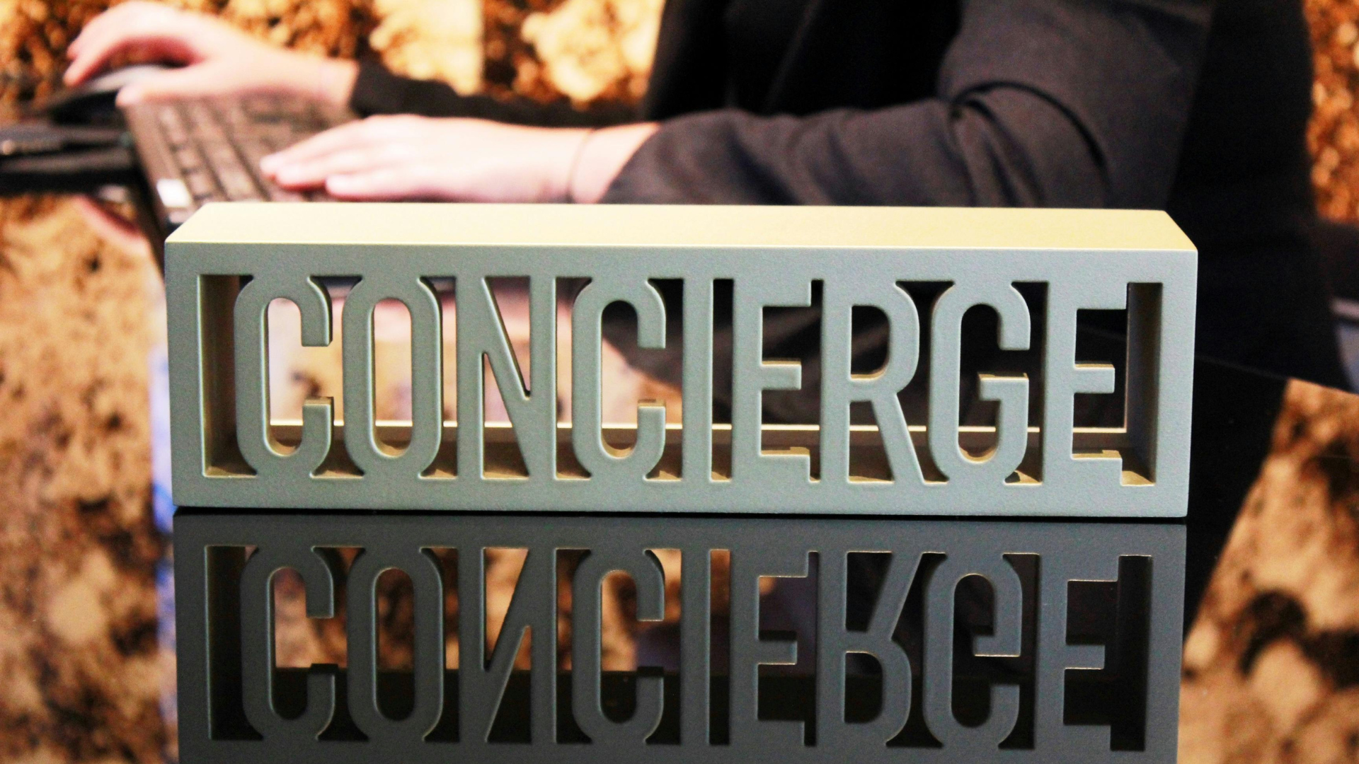 A person is typing on a laptop next to a sign that says concierge