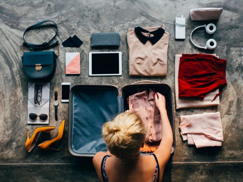 A woman is packing clothes into a suitcase on a table.