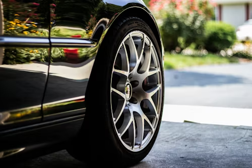 A close-up of a silver multi-spoke wheel on a shiny black car parked in a driveway.