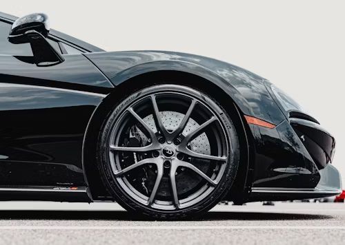 Black sports car front wheel, dark grey rim, black paint, parked on pavement.
