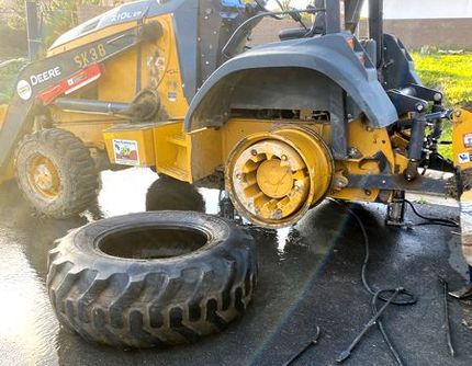 A yellow tractor with a tire on the ground next to it.