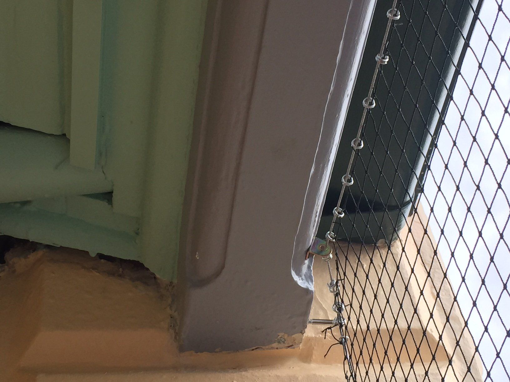 A bird cage is sitting on a wooden floor next to a window.