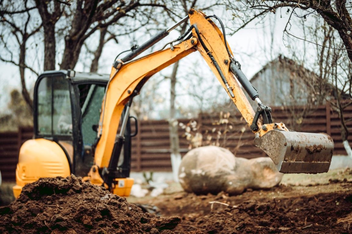 A yellow excavator is digging a large rock in the dirt.