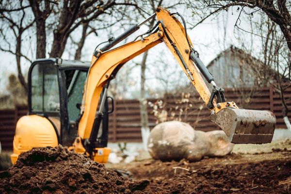 An excavator performing site prep is moving a large rock.