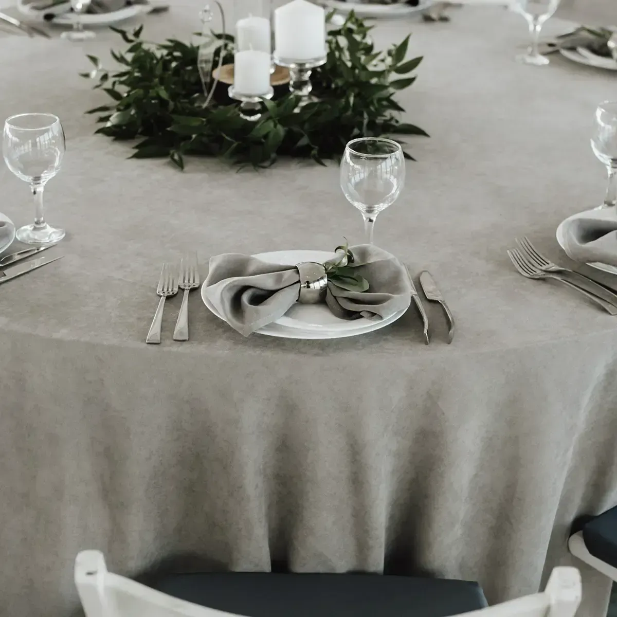 Elegant banquet table with gray linen, white plates, glassware, and a leafy candle centerpiece