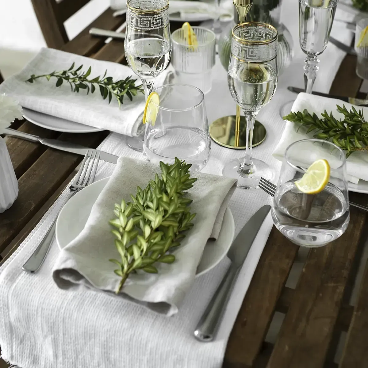 Elegant white table setting with green foliage centerpieces, wine glasses, and lemon garnishes