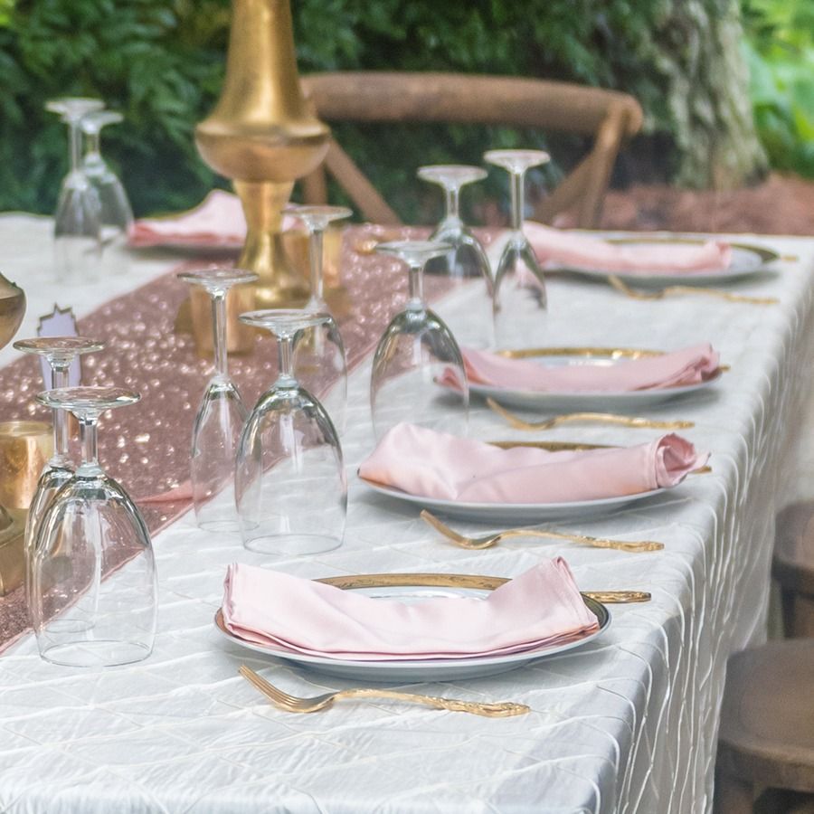 Elegant outdoor dining table set with pink napkins, upside-down glasses, and gold candleholders