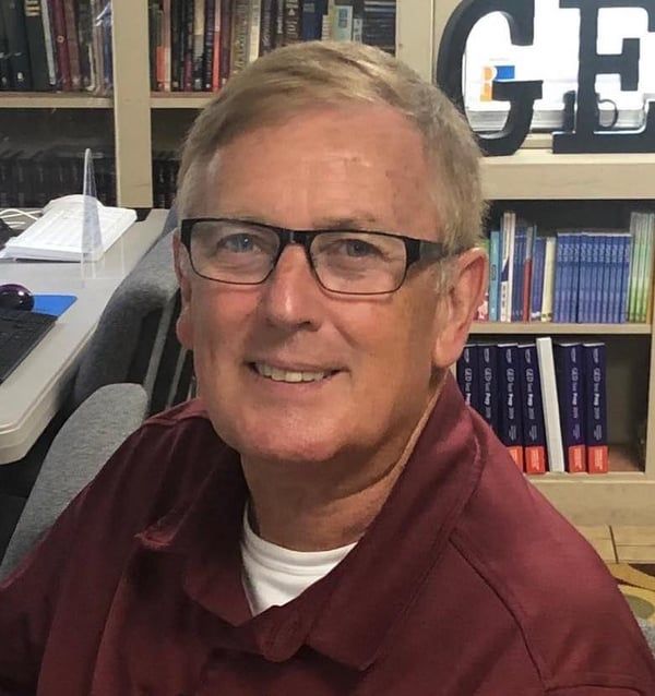 A man wearing glasses is smiling in front of a sign that says ge