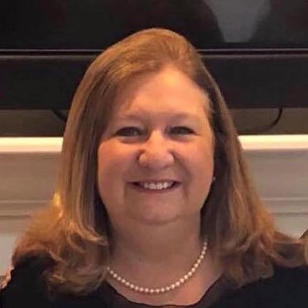 A woman wearing a pearl necklace and a black shirt is smiling for the camera.