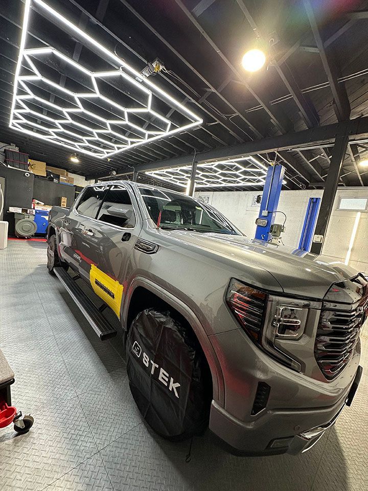 A gray truck is parked in a garage under a ceiling light.