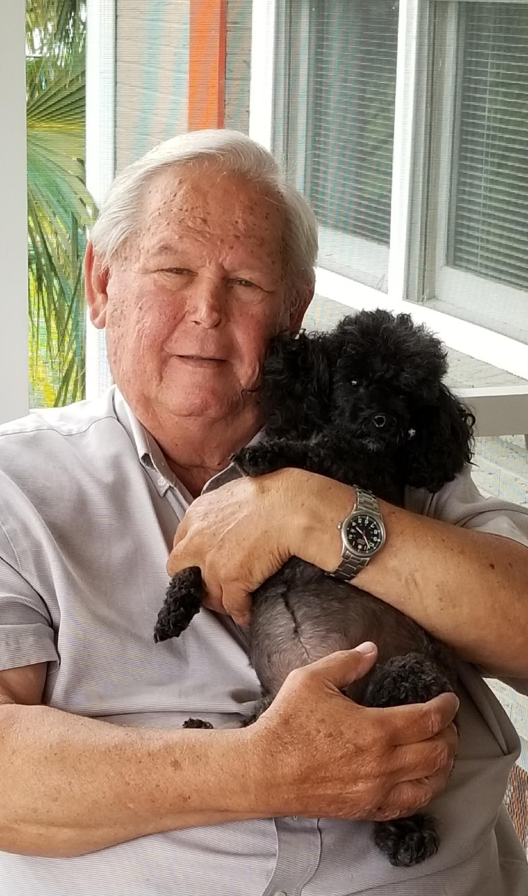 A man is holding a small black dog in his arms.