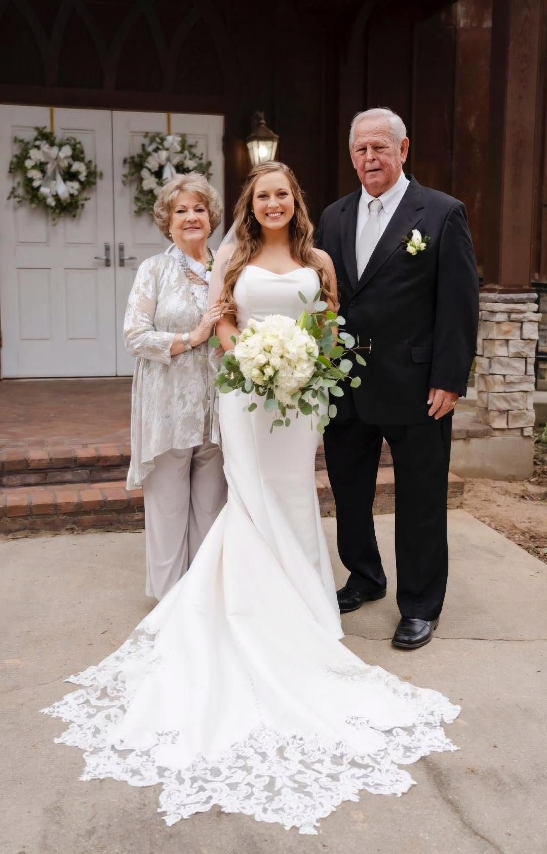 A bride and her parents are posing for a picture in front of a church.