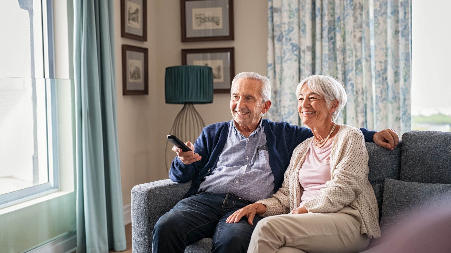 An elderly couple is sitting on a couch watching television.