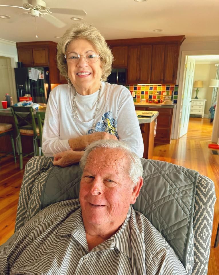 A man is sitting in a chair with a woman standing behind him.