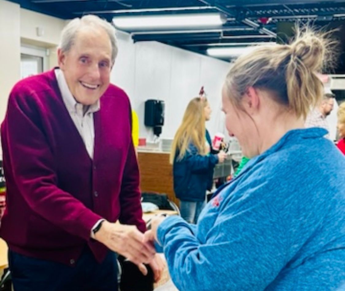 A man in a red sweater shakes hands with a woman in a blue sweater