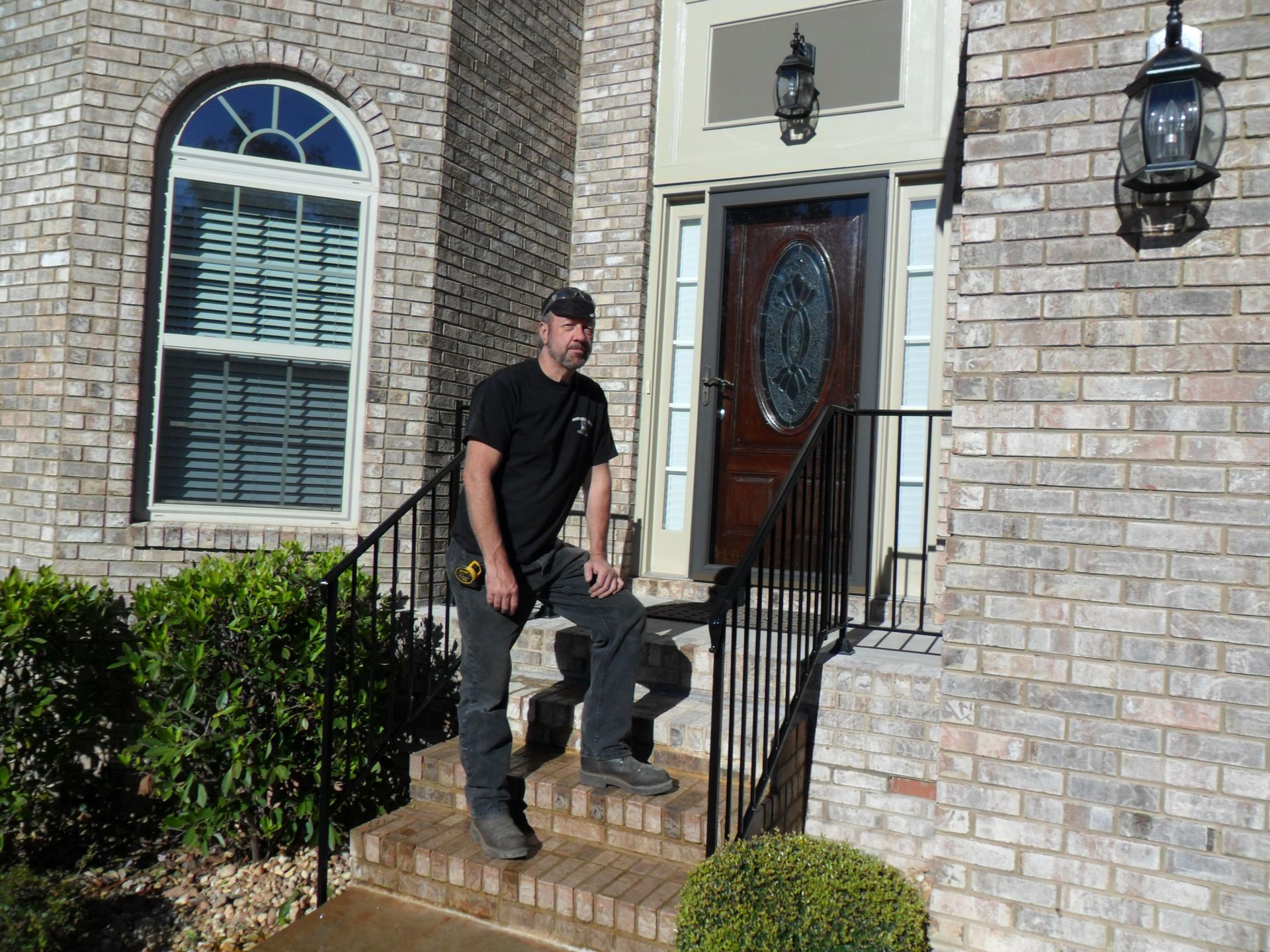 A man is standing on the steps of a brick house.