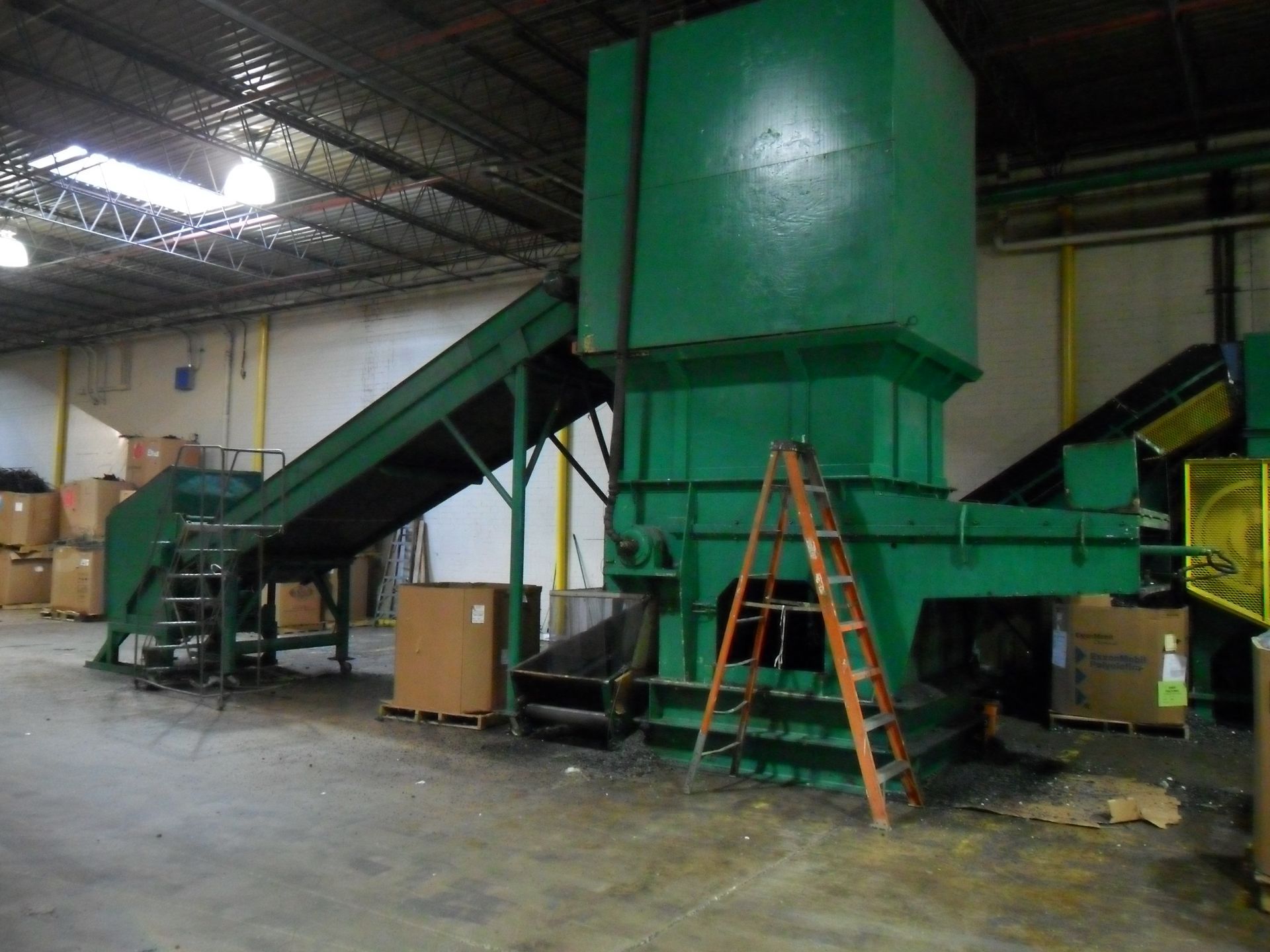 A large green machine in a warehouse with a ladder in front of it
