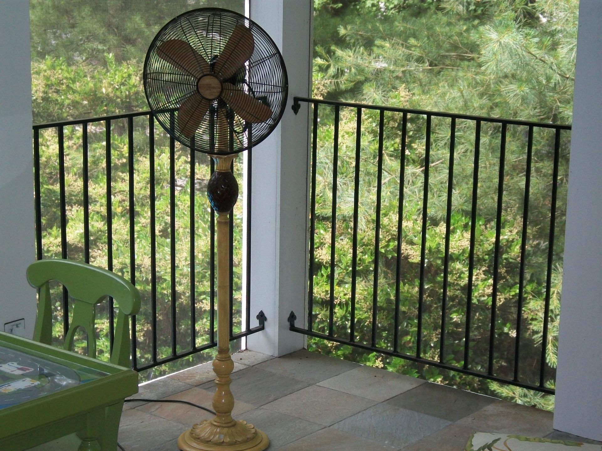 A fan is sitting on a porch next to a green chair