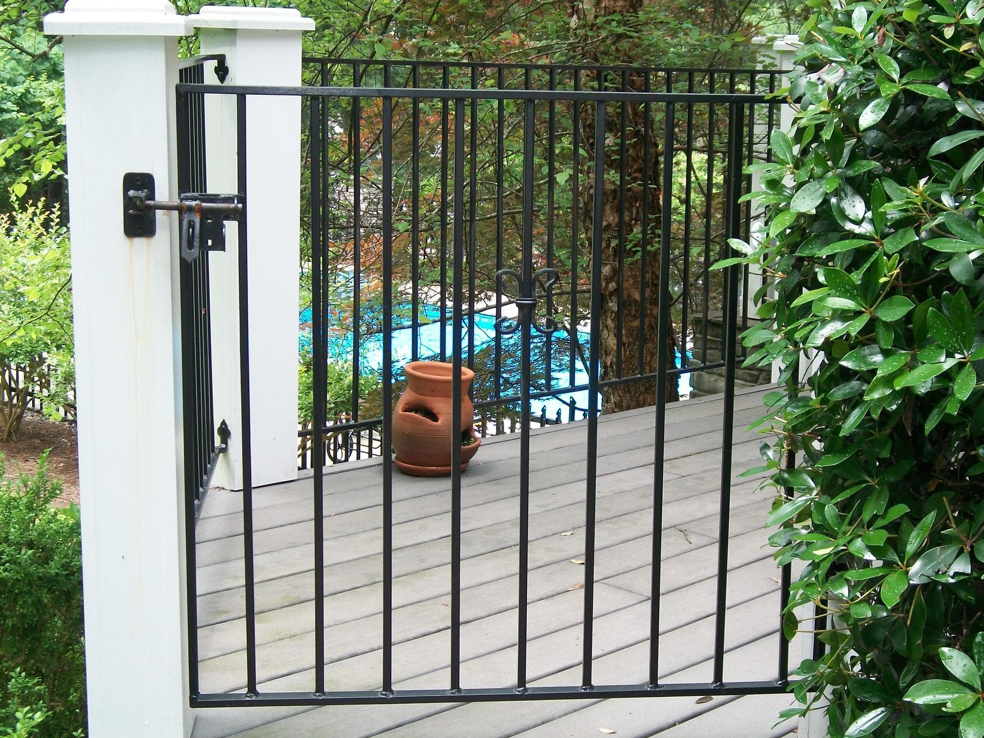 A black gate leading to a deck with a swimming pool in the background