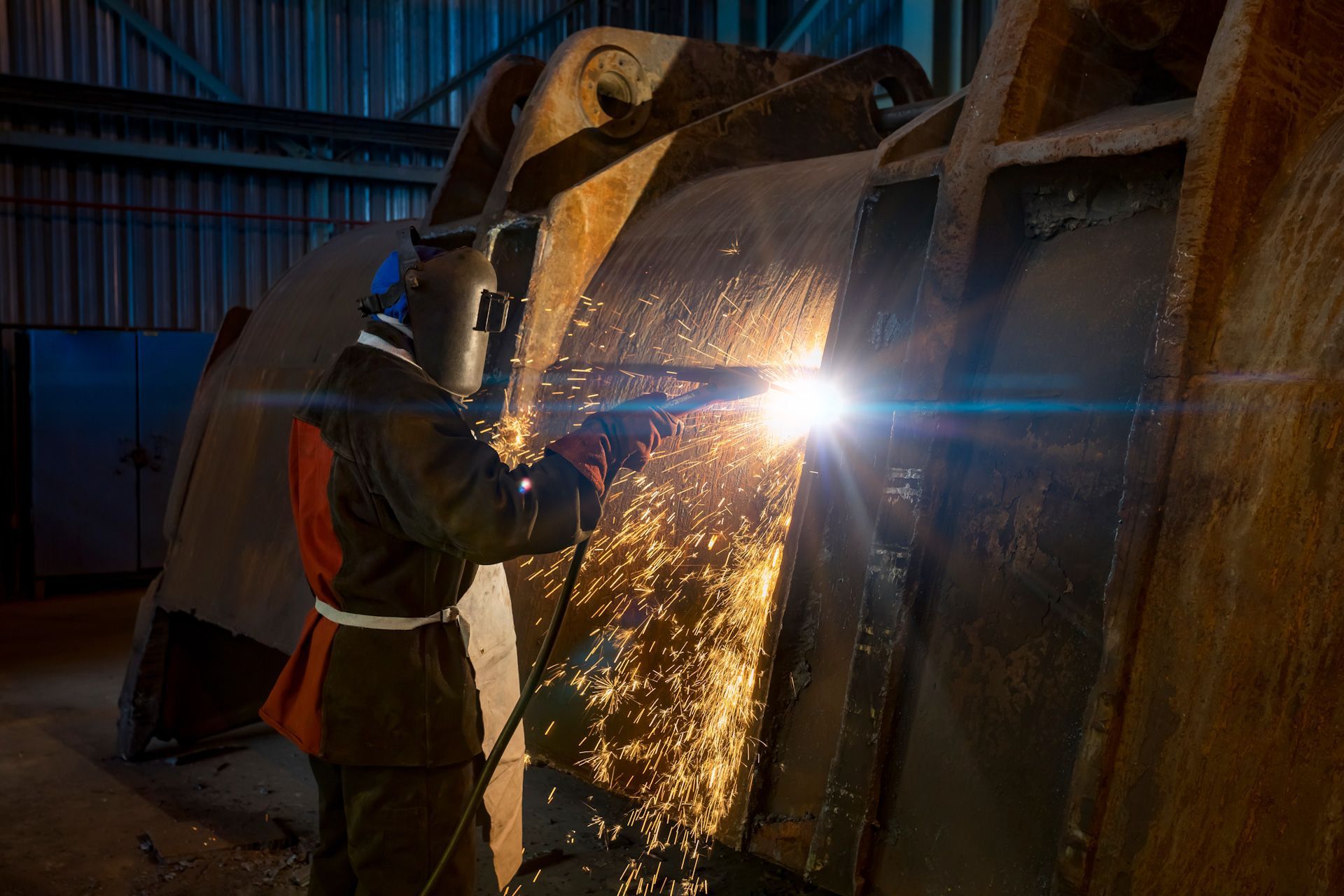 A man is welding a piece of metal in a factory.