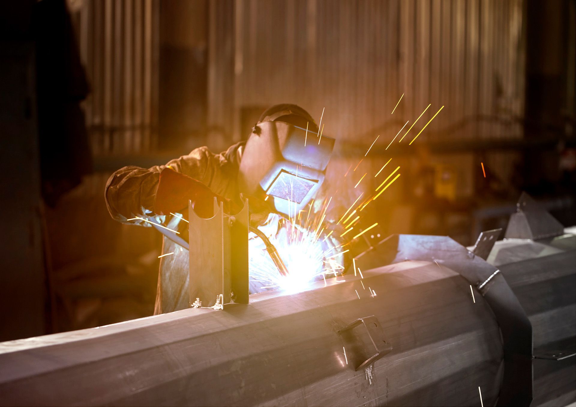 A man is welding a piece of metal in a factory.