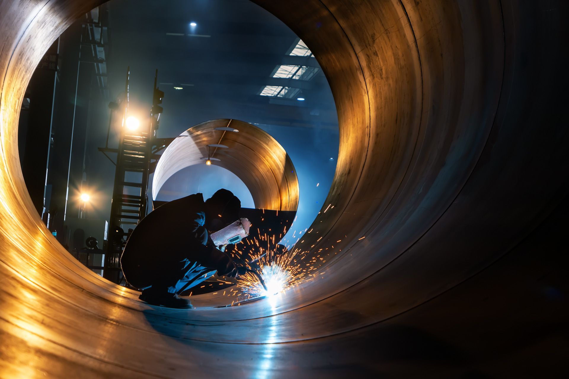 A man is welding a large pipe in a factory.
