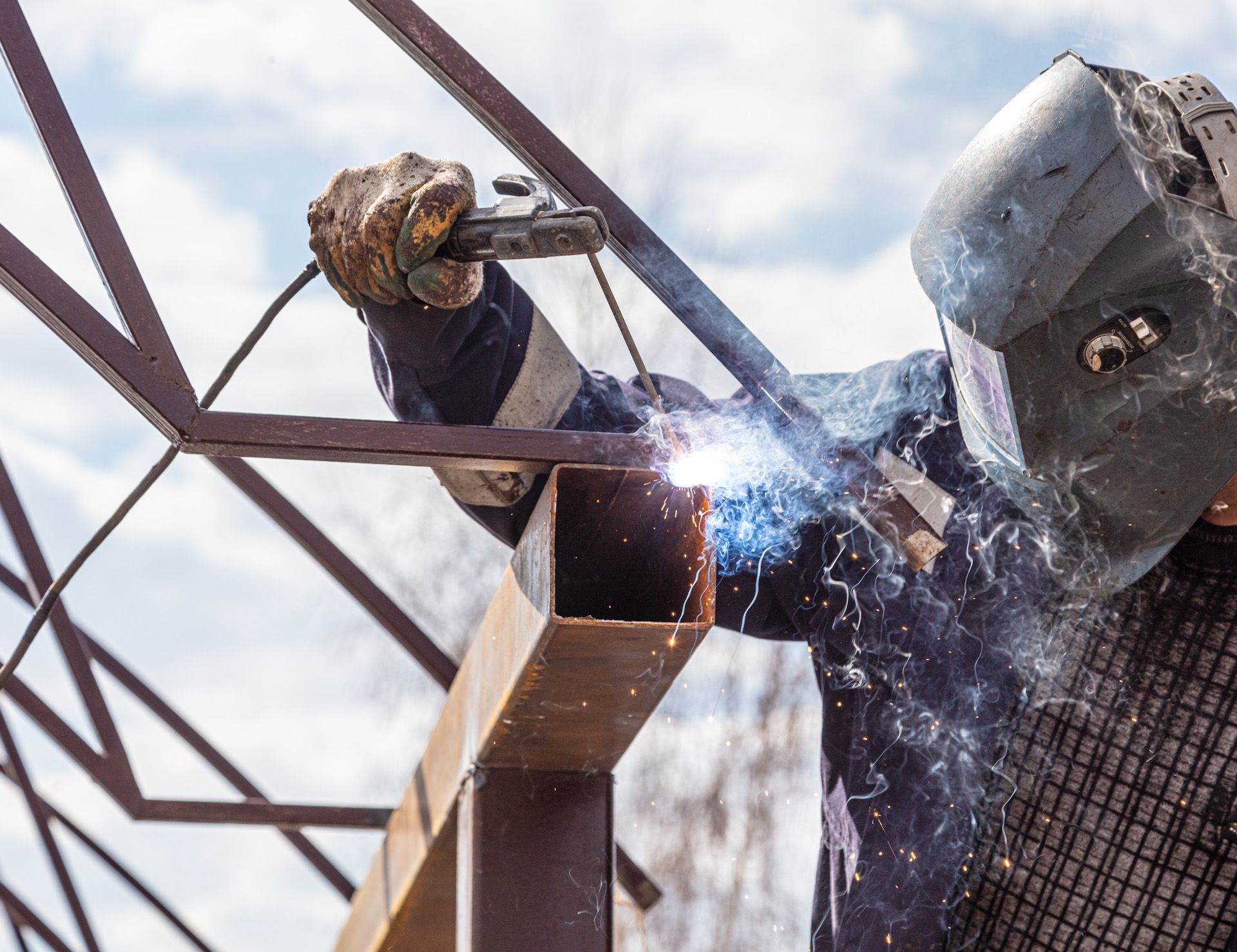 A man wearing a welding mask is welding a metal structure.