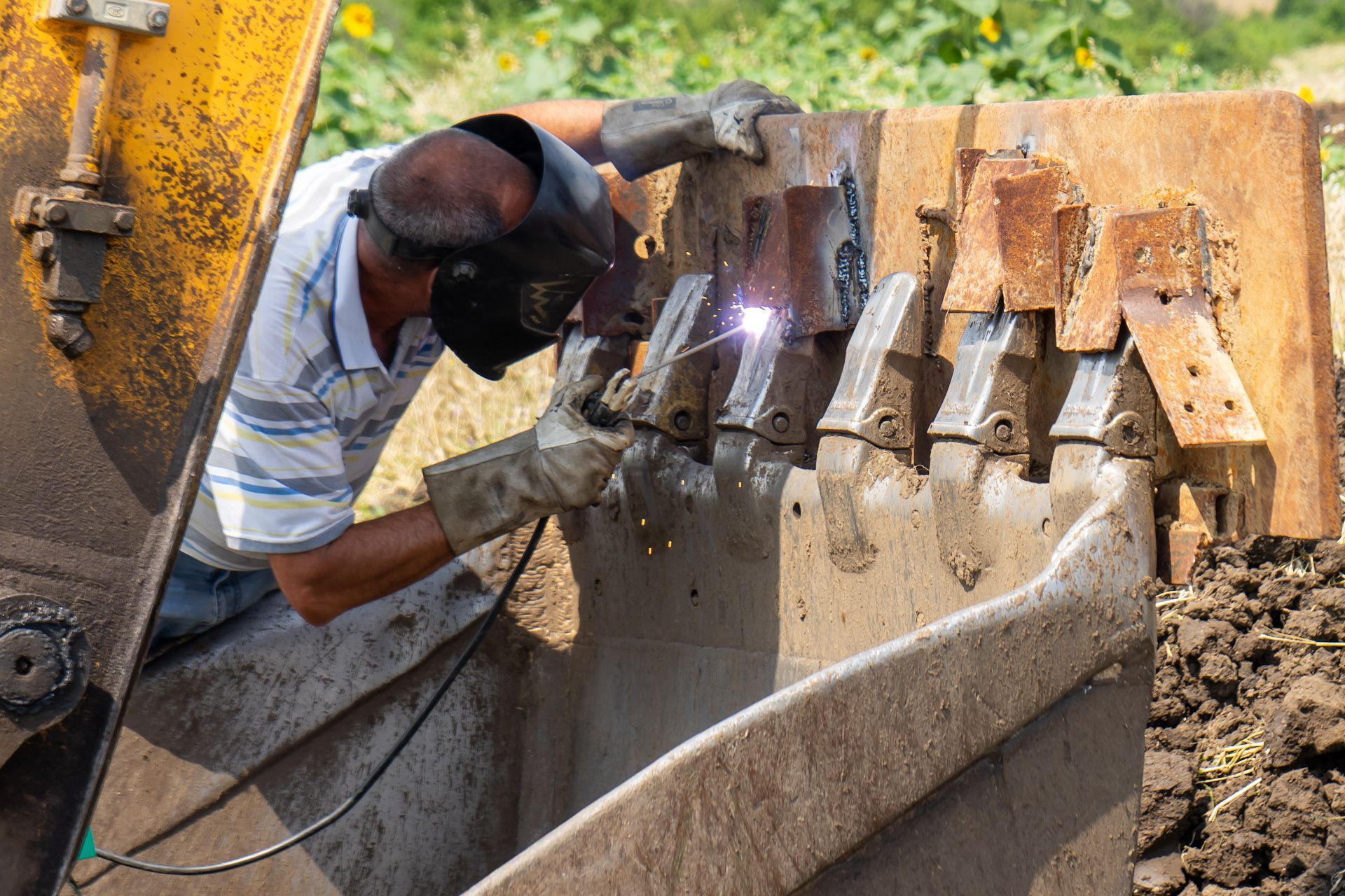 A man is welding a piece of metal on a bulldozer bucket.