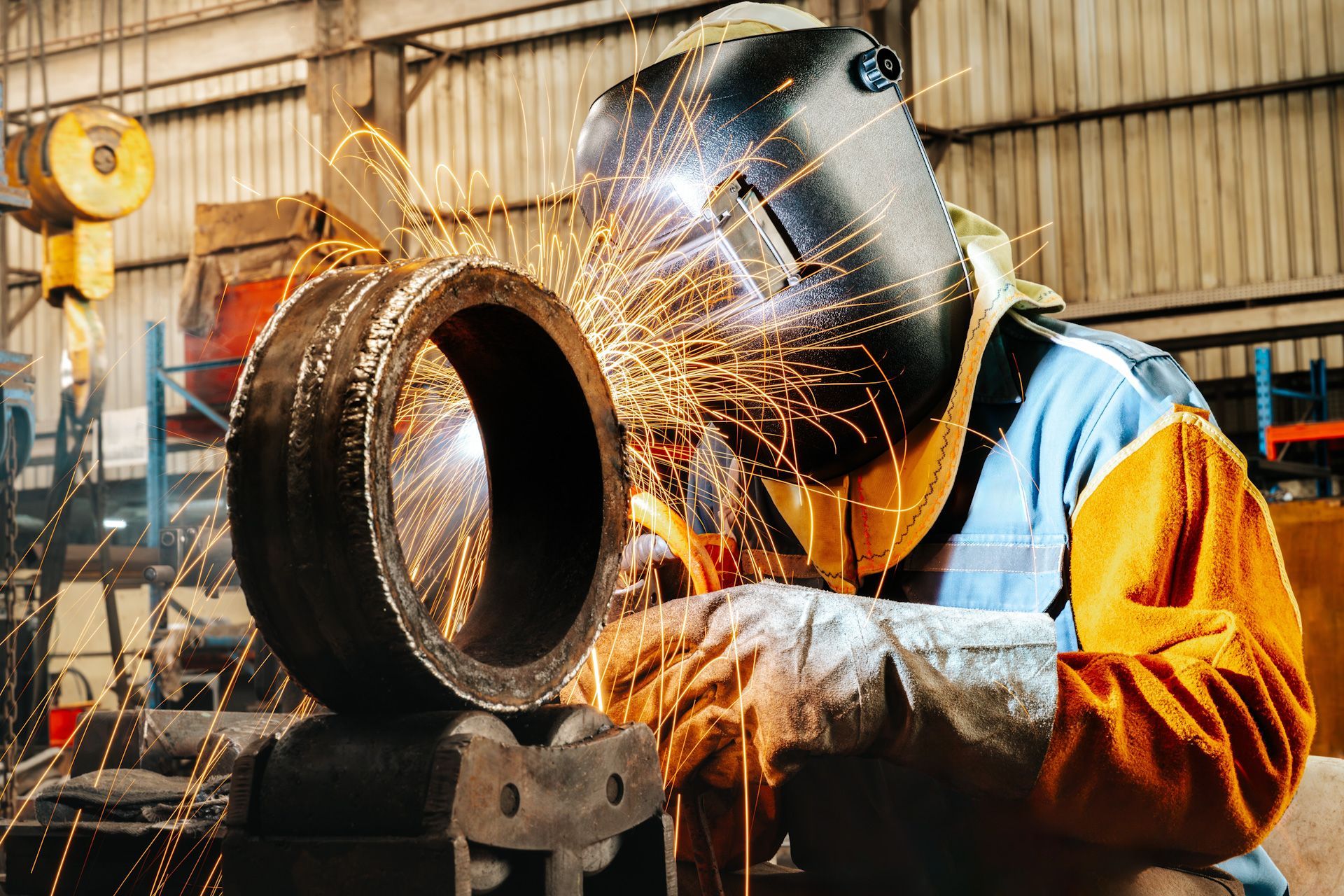 A man wearing a welding mask is welding a pipe in a factory.