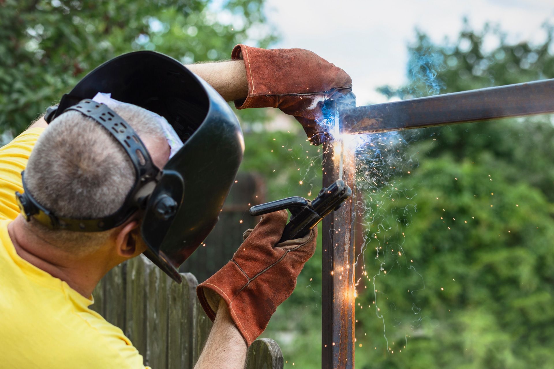 A man wearing a welding helmet is welding a piece of metal.