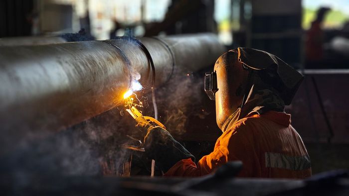 A man is welding a pipe in a factory.