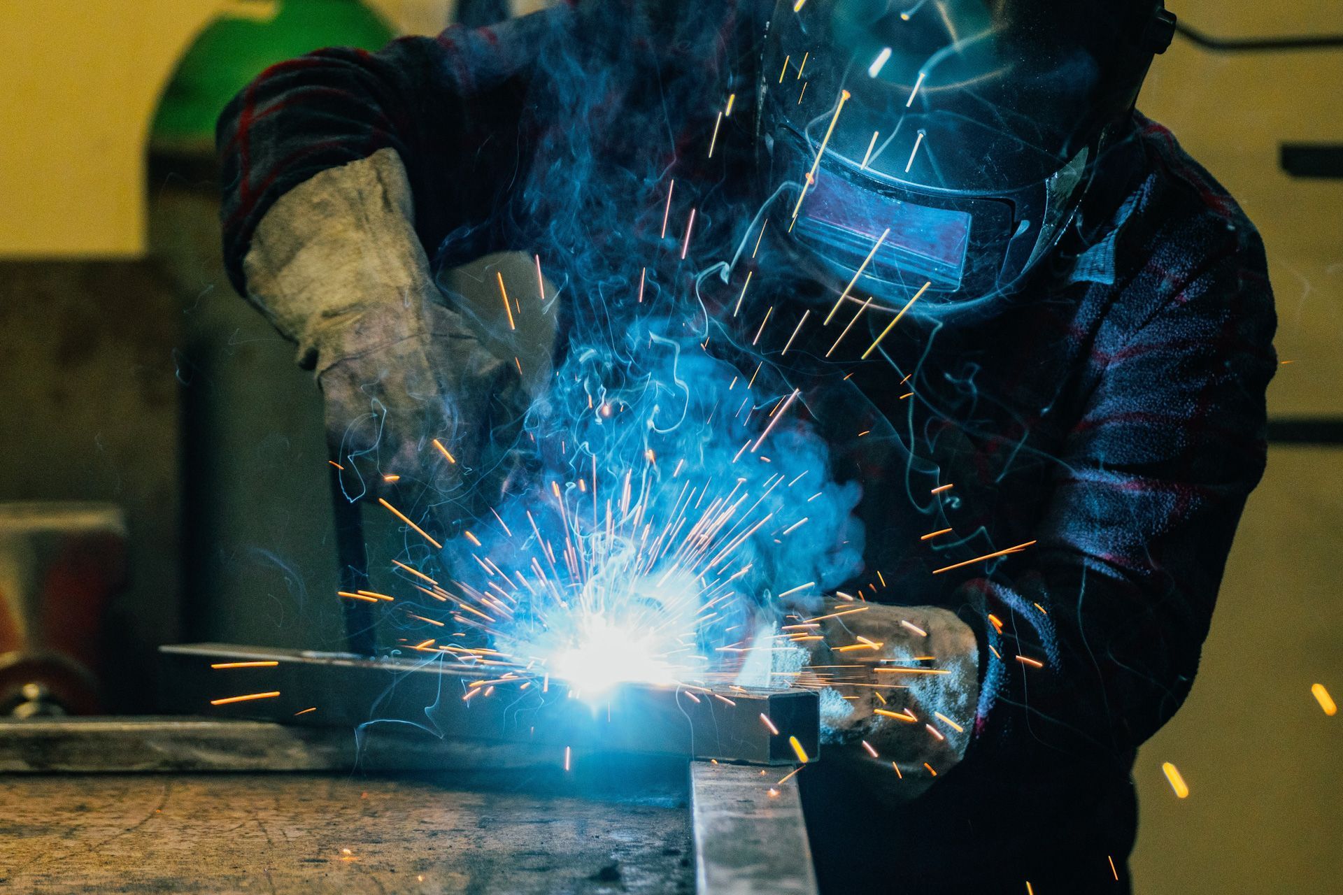 A man wearing a welding mask is welding a piece of metal.