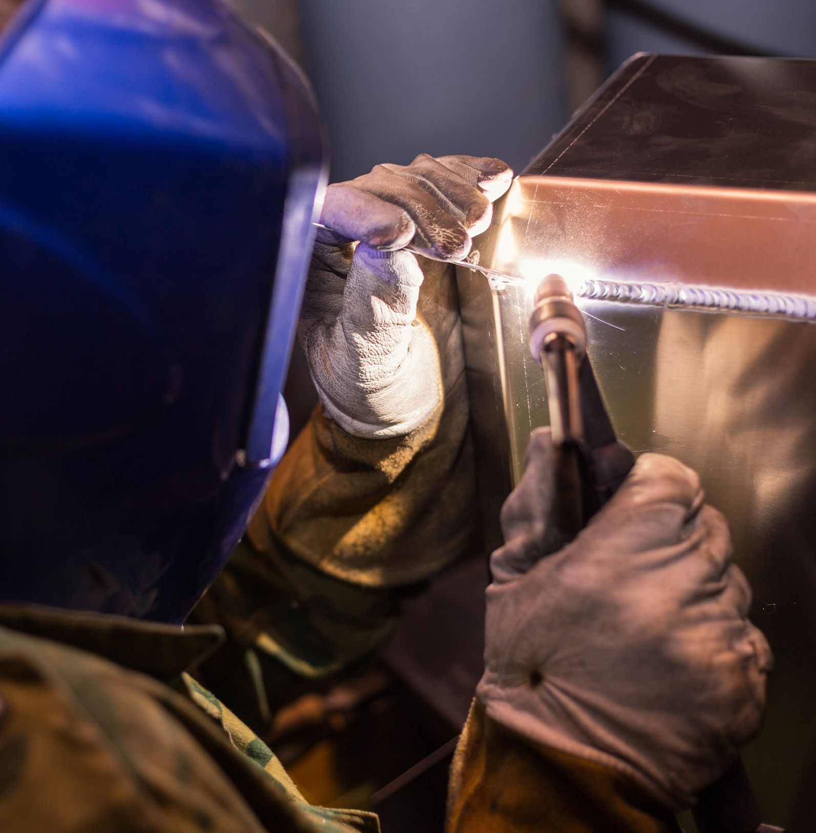 A man wearing a helmet and gloves is welding a piece of metal