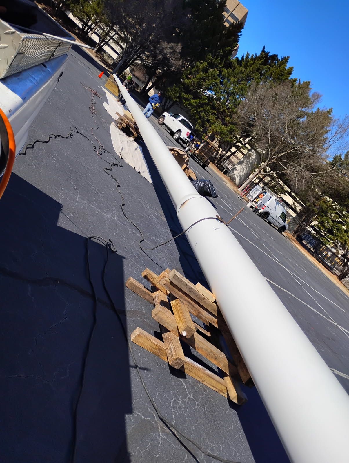 White pole lying across cracked street beside a parked car and wooden blocks, on a sunny road closure