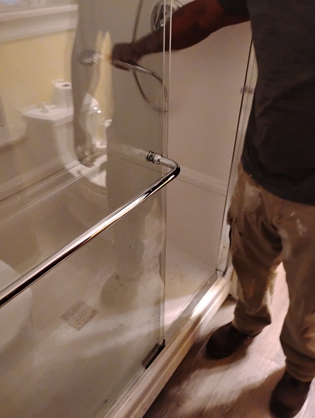 A man is working on a glass shower door in a bathroom