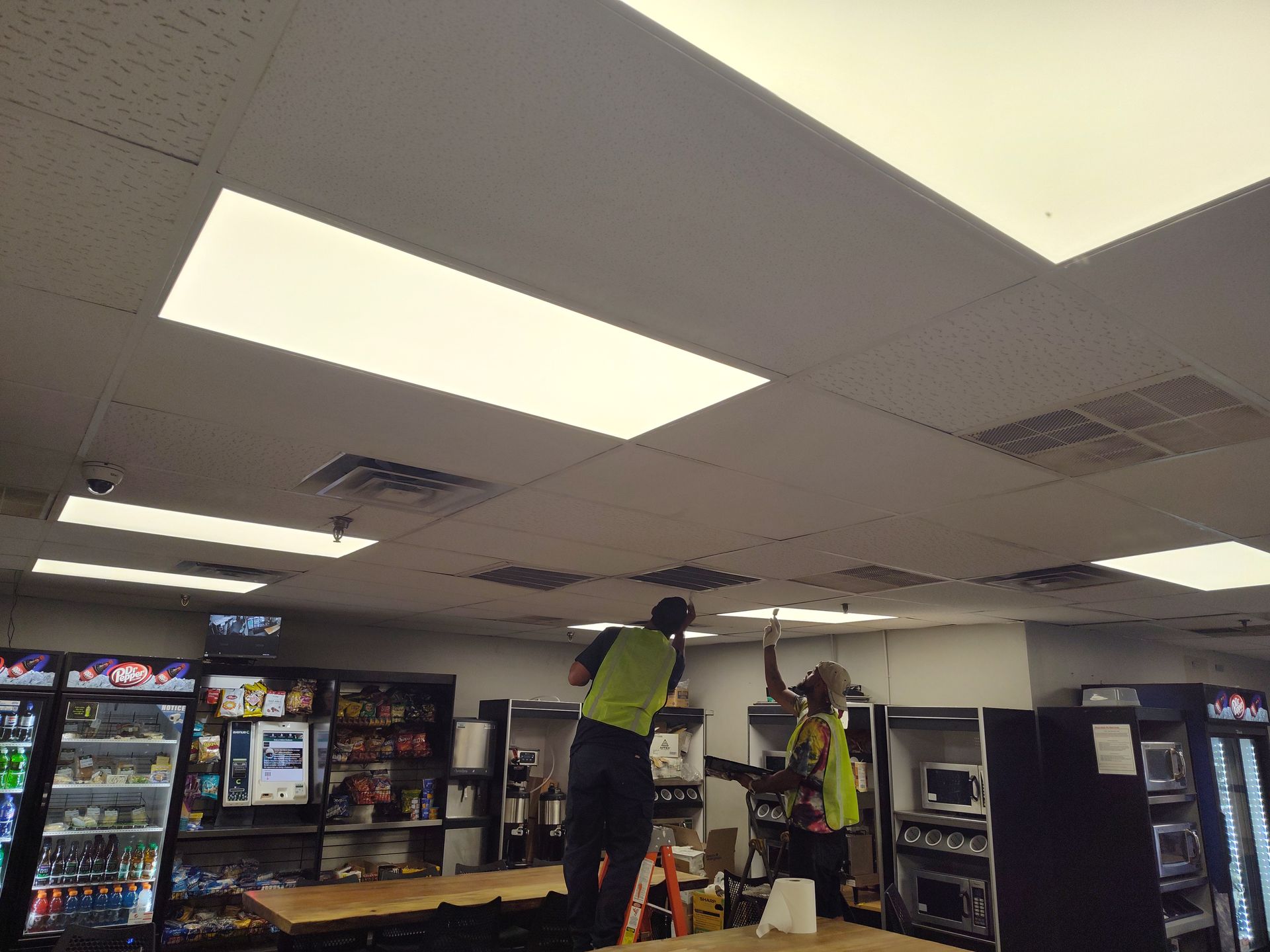 Two men are working on the ceiling of a building.