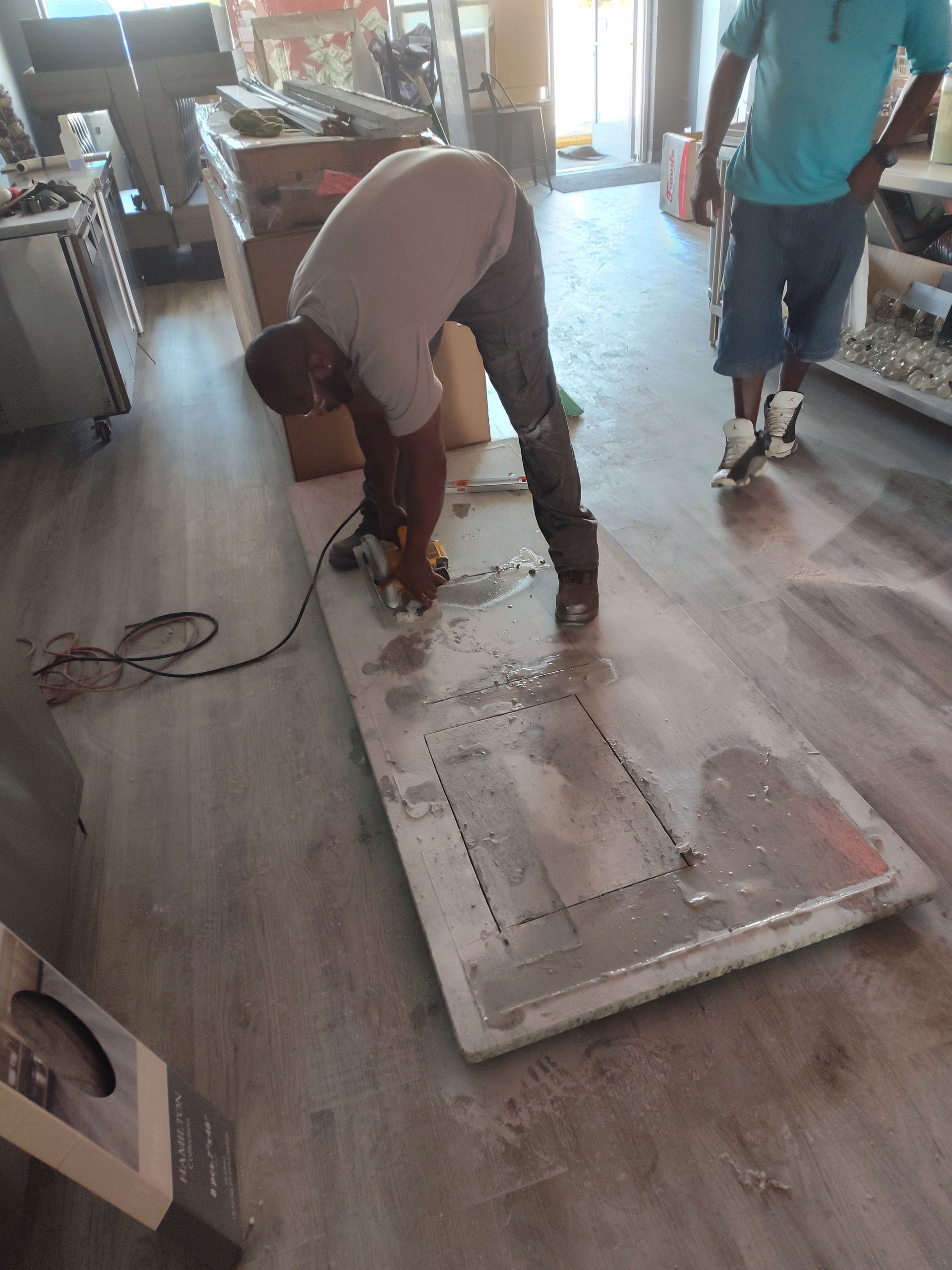 Two men are working on a large piece of wood in a living room.
