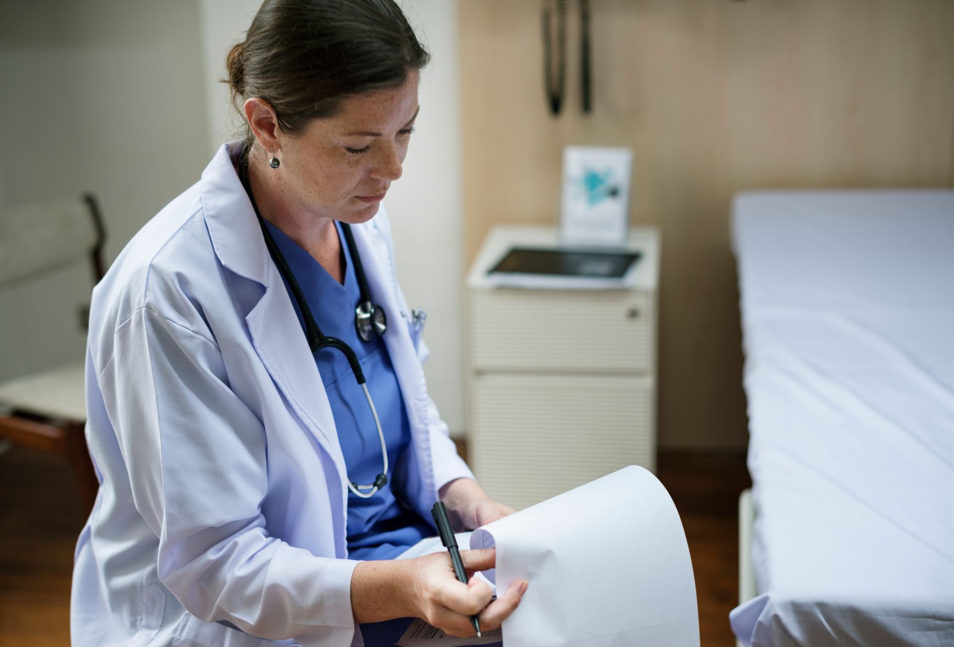 A female doctor is writing on a piece of paper in a hospital room.