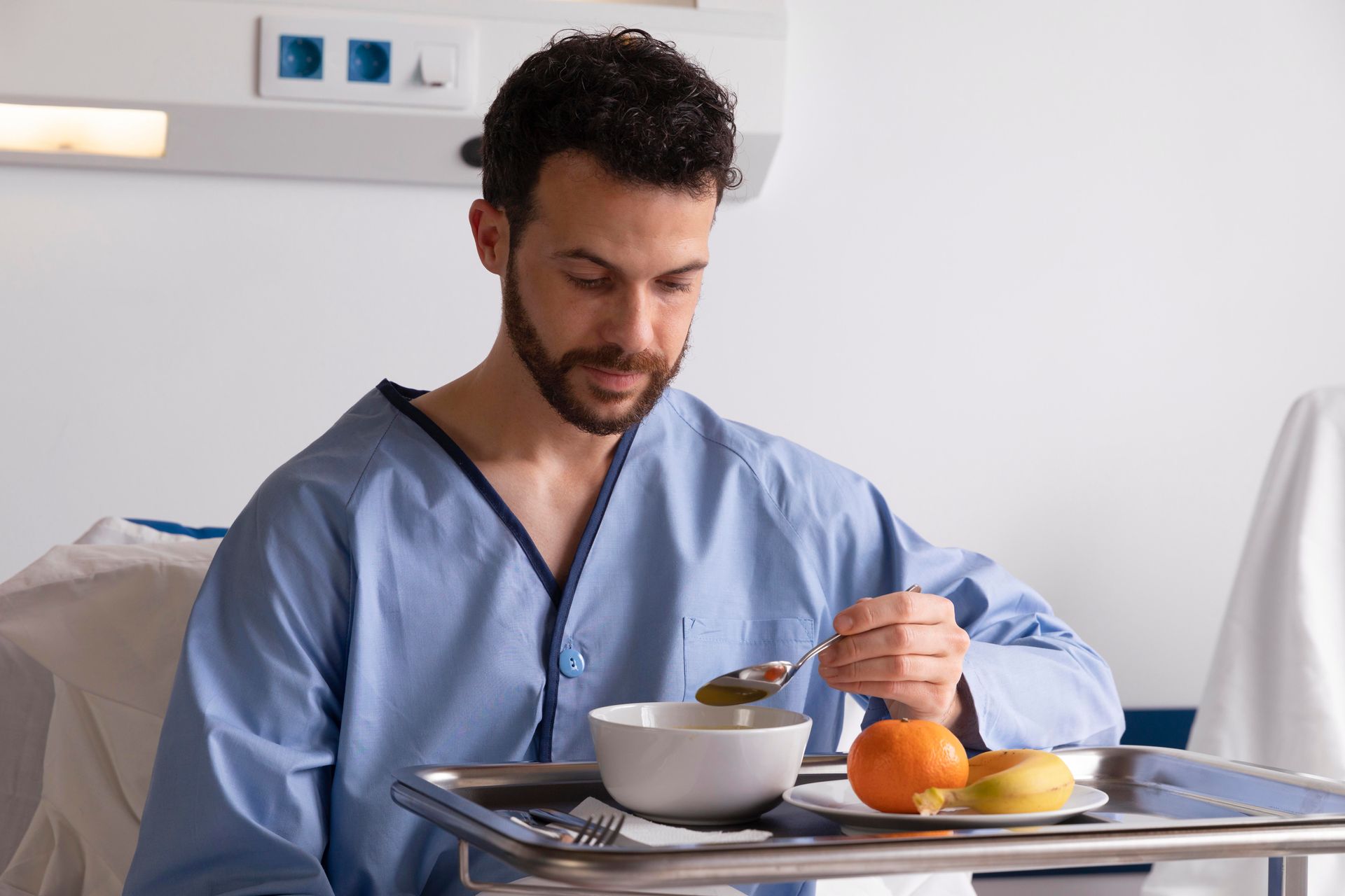 A man is sitting in a hospital bed eating food from a tray.